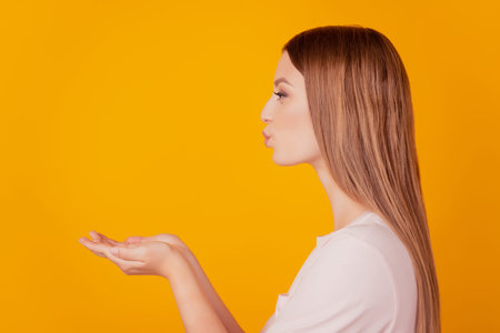 Profile portrait of sweet tempting blone lady look empty space hold palms blow air kiss on yellow...