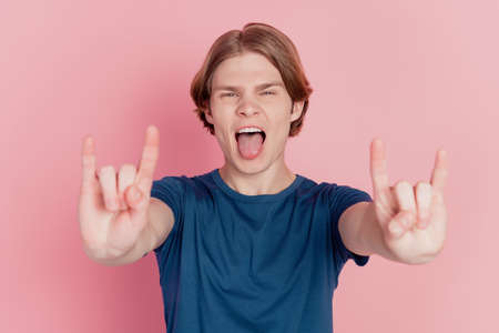 Photo of crazy excited guy happy positive smile show horns rock metal sign tongue-out brutal isolated pink color backgroundの写真素材