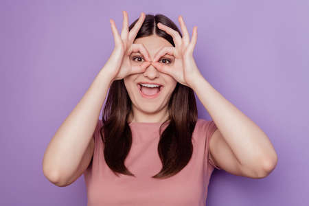 Photo of young attractive girl happy positive smile show fingers okay sign binoculars glasses isolated over violet color backgroundの写真素材