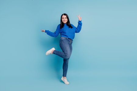 Full body photo of young cheerful girl dancing have fun disco music show peace cool v-sign isolated on blue colored backgroundの写真素材