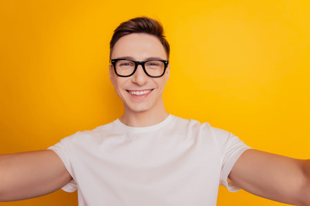 Portrait of handsome positive guy hold camera take selfie beaming smile on yellow backgroundの写真素材