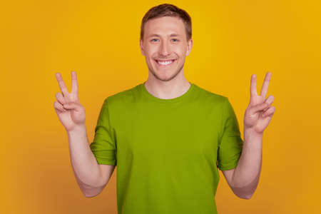 Photo of attractive positive cool guy raise hands make v-signs peace cool funky isolated on yellow color backgroundの写真素材