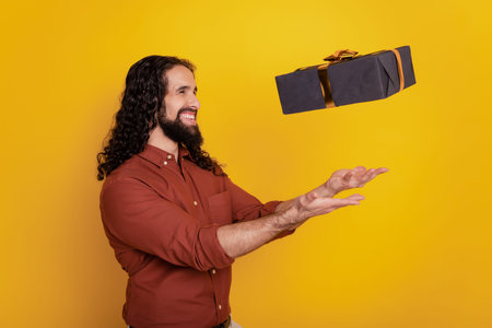 Portrait of cheerful handsome guy throw catch present box on yellow background
