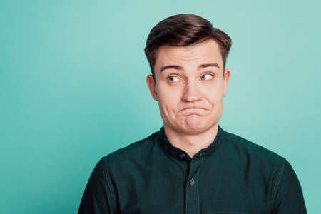 Portrait of uncertain clueless funny guy look side empty space grimace on turquoise backgroundの写真素材