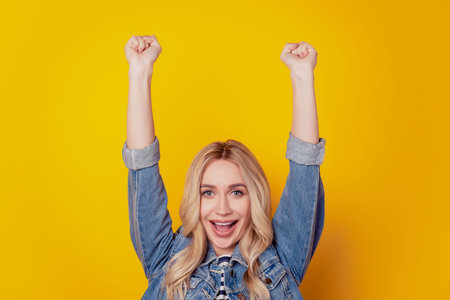 Portrait of astonished cute cheerful nice lady raise fists win concept on yellow backgroundの写真素材