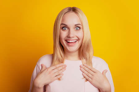 Portrait of shocked funny blonde girl hands chest look camera on yellow backgroundの写真素材