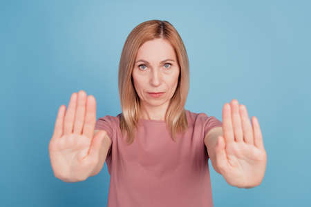 Portrait of serious unhappy confident woman holding two arms gesturing no sign isolated on blue color backgroundの写真素材