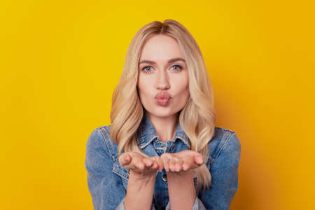 Portrait of dreamy affectionate nice lady hold hand blow air kiss look camera on yellow backgroundの写真素材