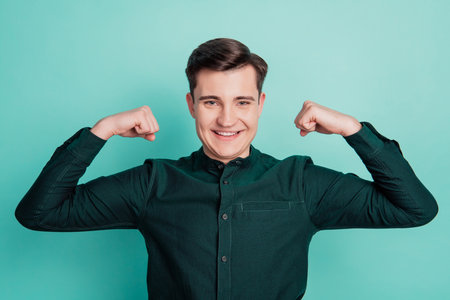Young business man show triceps arm muscle isolated on turquoise backgroundの写真素材