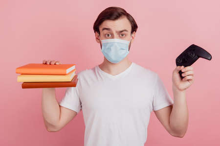 Photo of young man wear mask decide choice read book or play video game distance education home isolated over pink color backgroundの写真素材