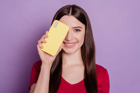 Portrait of charming cute positive lady hold phone cover eye on purple backgroundの写真素材