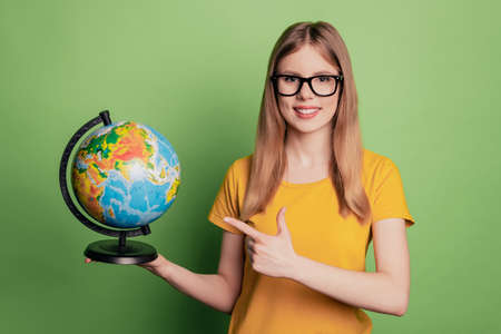 Portrait of reliable promoter cheerful lady direct finger globe choose country smile wear eyeglasses yellow t-shirtの写真素材