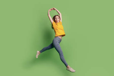 Portrait of elegant lovely shocked lady jump dance ballet wear yellow t-shirt jeans sneakers on green backgroundの写真素材