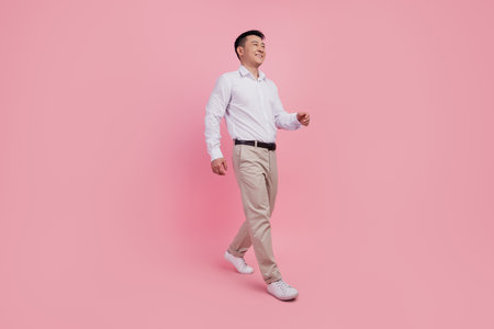 Full length profile side photo of young asian man go walk step look empty space isolated over pink color backgroundの写真素材