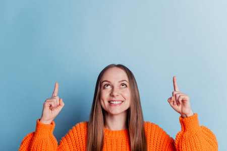 Photo of young cheerful girl point fingers empty space advertise choice promo isolated over blue...