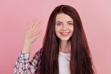 Photo of young cheerful girl good mood waving hand hello greetings symbol isolated on pink color backgroundの写真素材