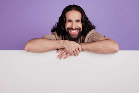Photo of cheerful latin man hands on placard billboard advertisement isolated on purple color backgroundの写真素材