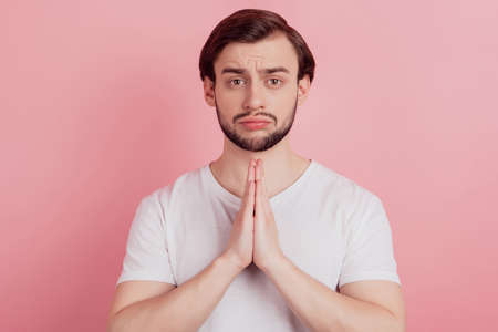 Portrait of nervous upset guy hold palms together cry ask help on pink backgroundの写真素材