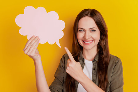 Portrait of positive charming nice lady direct finger hold mind bubble on yellow backgroundの写真素材