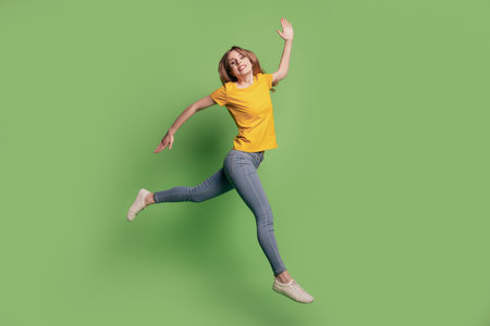 Portrait of careless dreamy funny lady jump run wear yellow t-shirt jeans footwear on green...