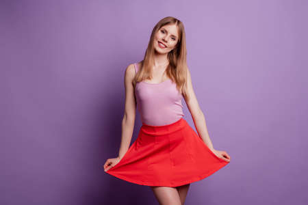Portrait of cute lovely pretty positive blonde lady posing wear pink top red short mini skirt on purple backgroundの写真素材