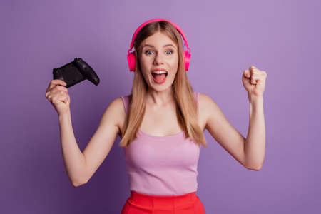 Portrait of cheerful astonished champion lady hold joystick open mouth wear headphones pink top on purple backgroundの写真素材