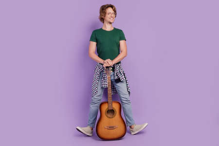 Full size photo of young guy happy positive smile guitarist look empty space isolated over violet color backgroundの写真素材