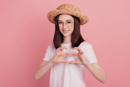 Photo of young attractive girl happy positive smile sunhat vacation show fingers heart symbol isolated over pink color backgroundの写真素材