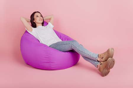 Full body profile side photo of young girl hands behind head relax free-time armchair isolated over pink color backgroundの写真素材