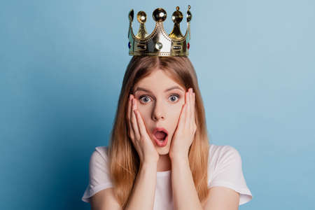 Photo of astonished cute shocked speechless princess lady wear golden crown open mouth on blue color backgroundの写真素材