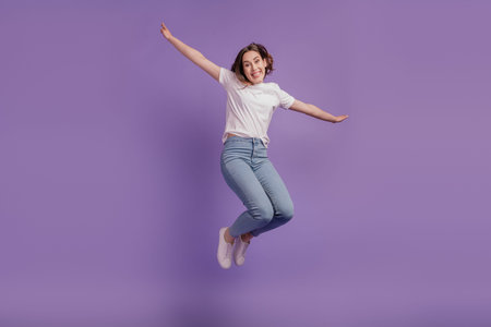 Full size photo of young cheerful girl jump up hands wings casual outfit isolated on violet color...