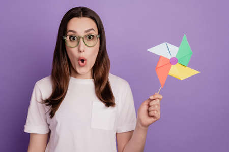 Portrait of excited young girl amazed shock surprised wow windmill toy isolated over violet color backgroundの写真素材