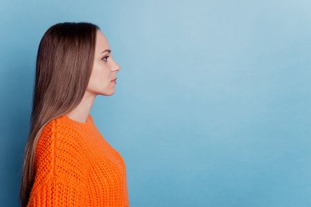 Profile side photo of young woman calm look empty space wear orange sweater isolated blue color backgroundの写真素材