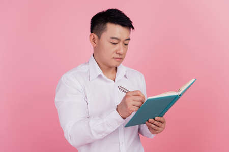 Profile side photo of young asian man write notes plan to-do list isolated over pink color backgroundの写真素材