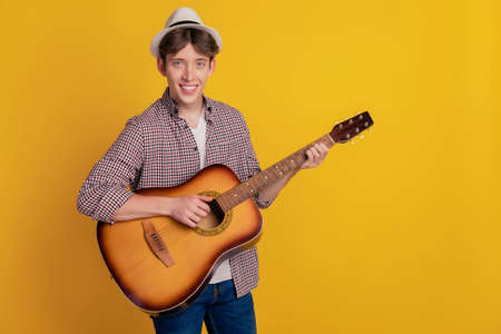 Photo of young cheerful man smiling playing guitar music lover acoustic isolated yellow color backgroundの写真素材