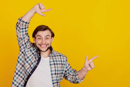 Portrait of handsome cheerful funky guy point fingers empty space ad advice choice isolated over bright yellow color backgroundの写真素材
