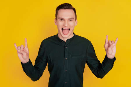 Photo of young crazy man tongue-out brutal show fingers rock sign isolated over yellow color backgroundの写真素材