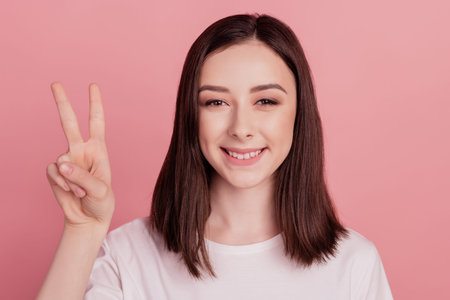 Photo of young attractive woman happy positive smile show cool peace v-sign isolated over pink color backgroundの写真素材