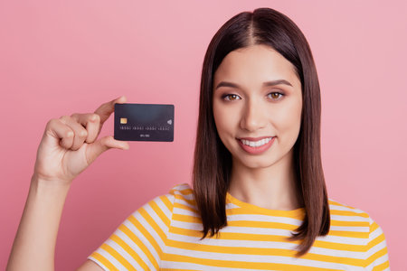 Portrait of cute positive cheerful lady demonstrate new banking service credit card on pink...