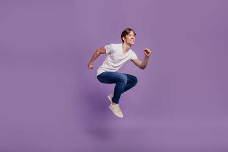 Full size profile side photo of young man have fun jump go run look empty space fast isolated on violet color backgroundの写真素材