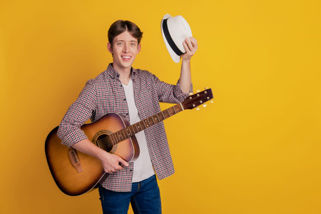 Photo of young cheerful man concert play guitar headwear performance isolated yellow color...
