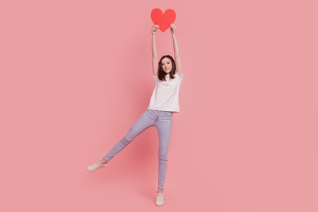Photo of pretty cute lady funny adorable mood raise hands hold red heart shape card isolated pink color backgroundの写真素材