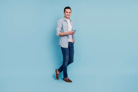 Full size profile side photo of young man go walk mobile type sms online isolated over blue color backgroundの写真素材