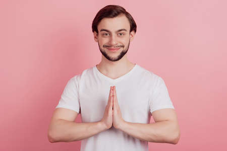 Portrait of charming pleading guy hold palms together look camera on pink backgroundの写真素材
