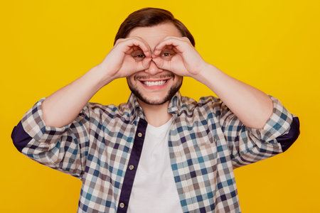 Photo of young cheerful excited man show fingers binoculars ok okey sign isolated over yellow color...