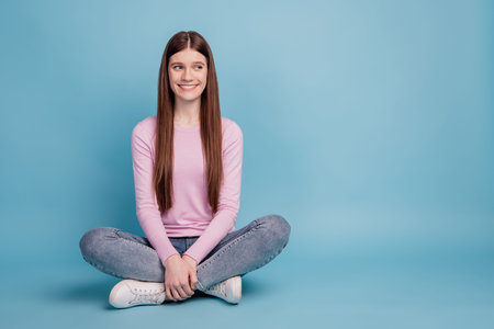 Full length photo of young girl happy positive smile sitting on floor dream look empty space isolated over blue backgroundの写真素材