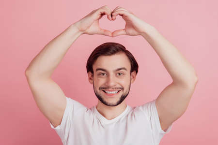 Portrait of cheerful affectionate nice guy show heart symbol raise hands on pink backgroundの写真素材