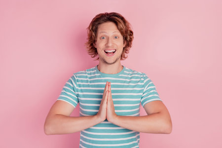 Photo of glad hopeful man hold hands together ask help wear casual blue striped t-shirt on pink...