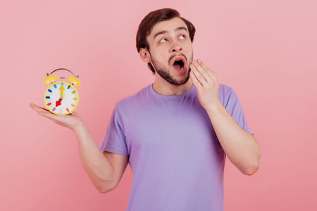 Photo of young man hold clock alarm syawn look empty space early morning isolated over pastel color...
