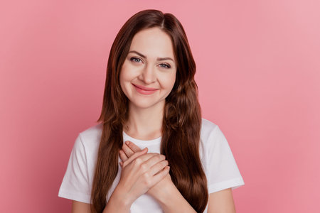 Portrait of grateful sincere girl palms heart chest look camera on pink background